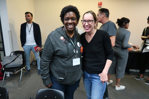 2 women standing together and smiling for a photo in a meeting