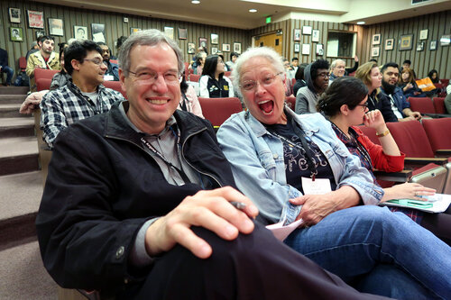 2 smiling people in the audience of a meeting